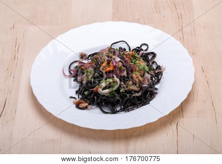 Black spaghetti with seafood and vegetables on wooden board