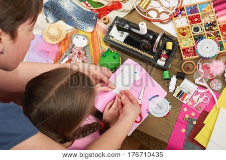 mother teaching daughter to sew doll clothes, top view, sewing accessories top view, seamstress workplace, many object for needlework, handmade and handicraft