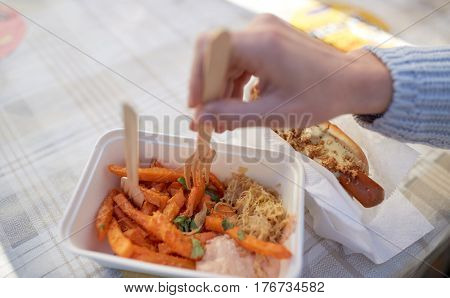 fast food, people and unhealthy eating concept - close up of hand with hot dog and sweet potato in disposable plate outdoors