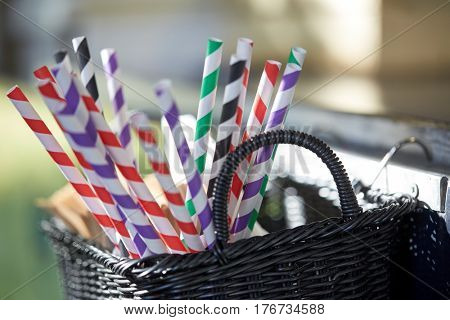 dishware and eating concept - disposable straws in whickered basket outdoors