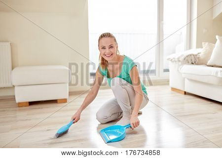 people, housework and housekeeping concept - happy woman with brush and dustpan floor at home