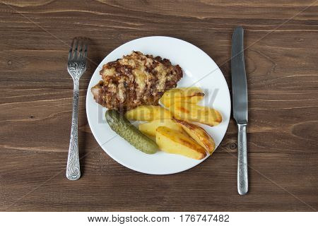 Grilled meat with potato and cucumbers on a wooden background