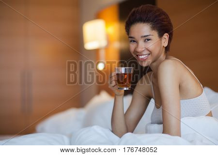 Young Happy Black Woman Sits In A Bed And Drink Tea.