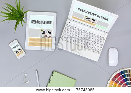 Working Place of web Designer on grey Table with responsive Site Theme on Laptop Tablet and Telephone Screens color Palette and green blank Page of Paper Notepad Top View flat Lay.