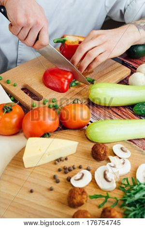 Cook cuts peppers on a wooden board. Cutting different vegetables on a wooden board. Tomatoes zucchini cucumber mushrooms