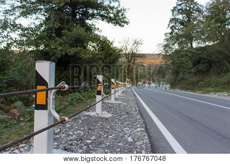 Road fence barrier. Canyon road with prominent tree and nice blue sky. Close up asphalt road texture with white stripe