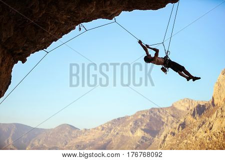 Rock climber pulling himself up using rope to reach quickdraws on cliff in order to remove them