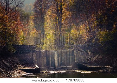 Autumn colors in the forest and a stone man made waterfall touched by the sunlight