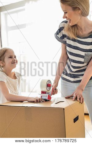 Mother and daughter looking at each other while packing cardboard box at home