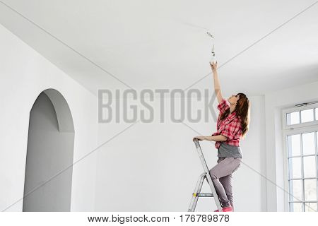 Full-length of woman on ladder fitting light bulb in new house