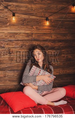 Cute girl sitting with a pillow in a Christmas interior with a pillow in her hands glowing lamps/ Let it snow is inscription on the pillow