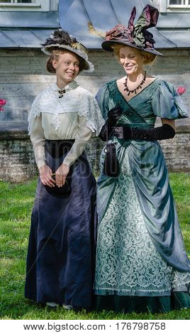Saint Petersburg, Russia - may 15, 2016: Actors demonstrate vintage clothing 19 century in the Park
Two young women in vintage dresses of the 19th century and hats posing on a background of green meadows and facade of the house