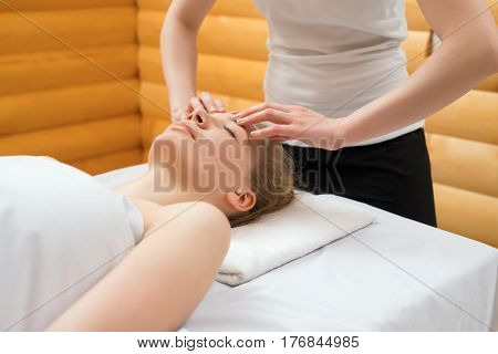 Close-up shot of therapist doing face massage to female client at spa center. Woman lying on desk at salon and enjoying facial massage at spa resort