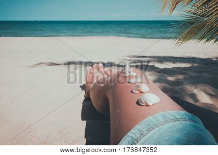 Relaxation and Leisure in summer - Seashell on tanned girl leg at tropical beach in summer. vintage color tone