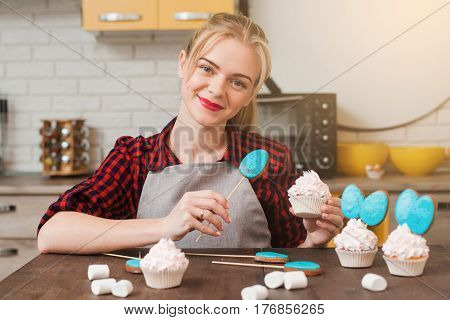 Young smiling woman cooking homemade cup cakes in kitchen. Culinary masterpiece. Easter gift, small business, delivery of sweets, craftmanship concept