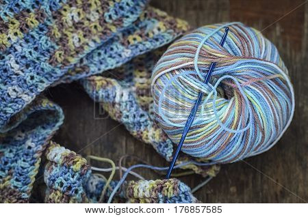 Knitting a scarf from a multi-colored six on a wooden background. Multicolored pattern, warm, cozy.