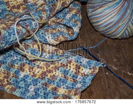 Knitting a scarf from a multi-colored six on a wooden background. Multicolored pattern, warm, cozy.