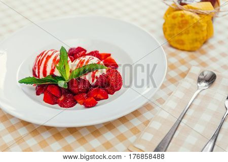Strawberry ice cream dish with fresh strawberry and green petal serve on decorated with checkered cloth table