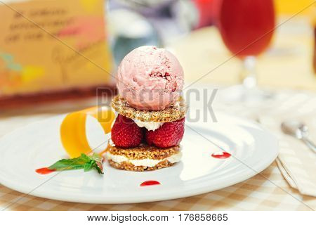 Strawberry ice cream dish with fresh strawberry, fresh cookie and green petal serve on decorated with checkered cloth table