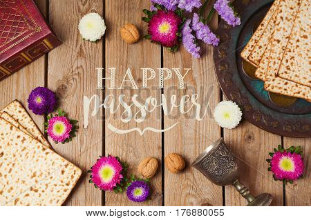Jewish holiday Passover greeting card with matza and seder plate over wooden background. View from above