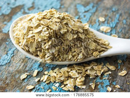 raw oatmeal is scattered on the desk of the bank in which the oat flakes are stored. blue background in the style of Shabby Chic. white spoon with uncooked oatmeal