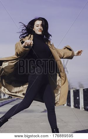 stylish young woman out for a walk. she dressed and looks very fashionable. coat of beige (camel) color and black turtleneck. beautiful woman. She jumps to the side and her hair fly.