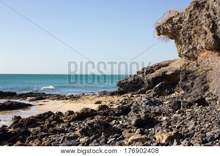 Black rocks of Costa Calma beach. Blue sea line. Playa Barca, Fuerteventura, Canary islands, Spain. Istmo de la pared view