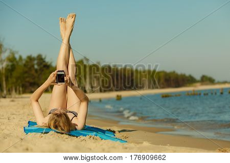Summertime pleasures enjoying vacation concept. Woman in bikini sunbathing and relaxing on beach using smartphone checking social media and writing sms