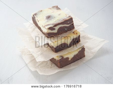 Pile of three marble chocolate brownies. Homemade dessert upon parchment. Square pieces of brownie cheesecake. Selective focus on the front.