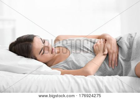 Young woman suffering from abdominal pain while lying on bed at home. Gynecology concept