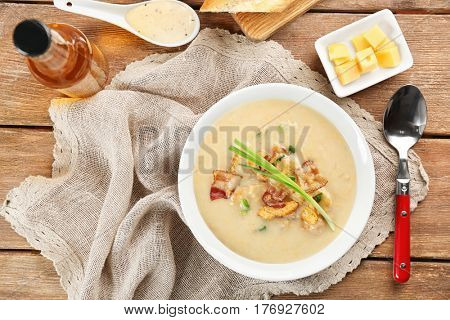 Delicious beer cheese soup with onion and fried bacon on table