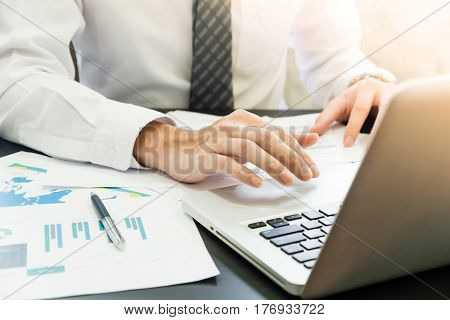 Close up of Businessman analyzing investment charts and using laptop on the desk.