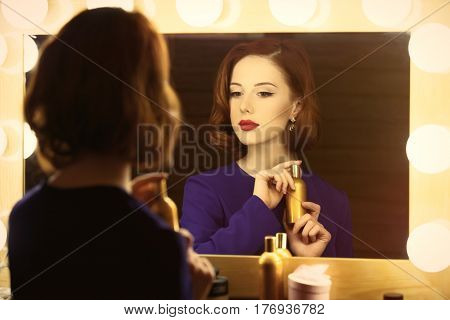photo of beautiful young woman holding her perfume near the window with lights