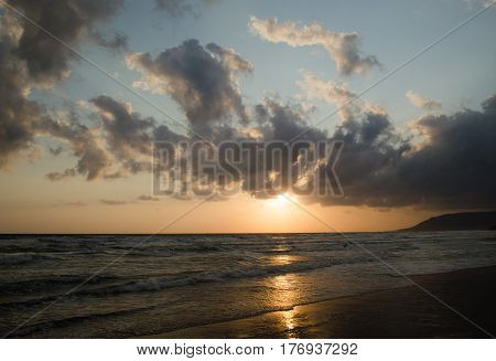 Sunrise over the sea, the rolling calm waves,  horizon is orange, skay orange and blue, clouds are grey and pink.