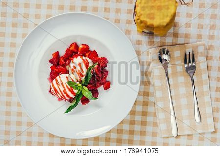 Strawberry ice cream dish with fresh strawberry and green petal serve on decorated with checkered cloth table