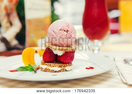 Strawberry ice cream dish with fresh strawberry, fresh cookie and green petal serve on decorated with checkered cloth table