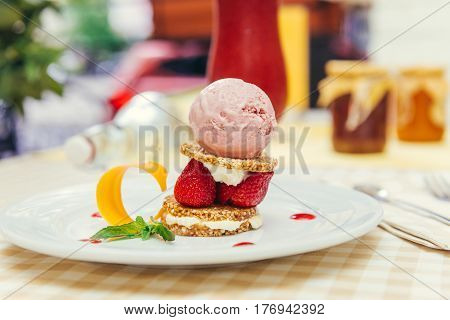 Strawberry ice cream dish with fresh strawberry, fresh cookie and green petal serve on decorated with checkered cloth table