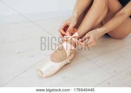 Conceptual image of a ballet. The ballerina tie the pointes. Woman dancer at a training session. Ballerina. Preparing for the competition. Classes in single sports.