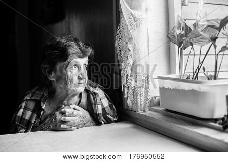 An elderly woman pining at the window. Black-and-white photo.