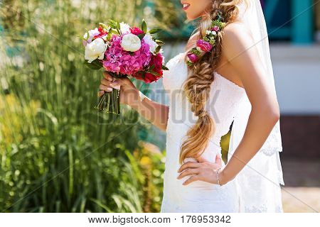 Bride holding delicate and tender marriage bouquet in white and pink colours with green petals. Beautiful sunny day in park.
