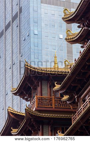 Juxtaposition of old versus new architecture styles: modern skyscraper towering above a traditional chinese building