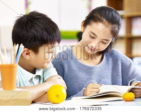 asian elementary school girl and schoolboy studying together in classroom.