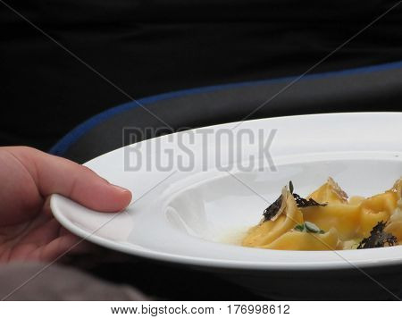 Chef holding cooked handmade Agnolotti to serve in the restaurant . Typical italian egg pasta on white plate