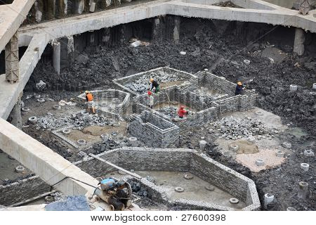 Cantiere, muratori, costruzione di muro di mattoni di un tappi tubo di cemento in un seminterrato di un multipiano b
