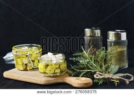 Marinated Feta In A Glass Jar And Spices On A Black Background.
