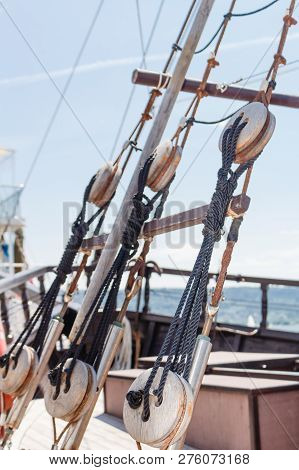 View On Part Of Old Wooden Sailboat With Bright Blue Sky Background. Old Deadeye With Cables On The 