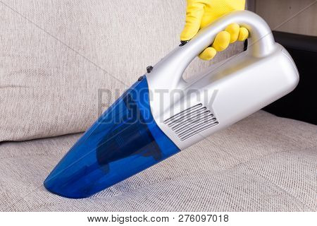 Person With Protective Gloves Hoovering Sofa With Handheld Vacuum Cleaner