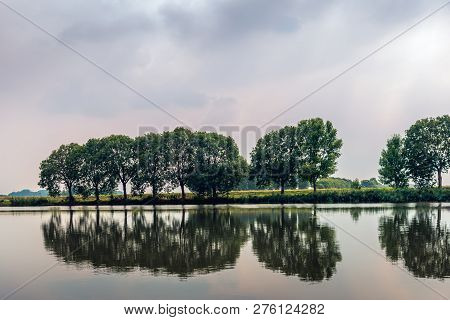 Row Of Trees Reflected In The Mirros Smooth Water Surface Of A Dutch Lake In The Summer Season.