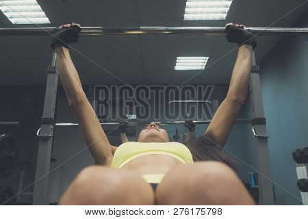 View To The Legs And Breast Of Sportswoman Lying On The Bench And Lifting Barbell At Gym Hall Backgr