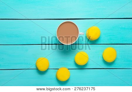 A Cup Of Coffee And Yellow Macaroons On A Blue Wooden Table. Trend Of Minimalism. Top View.